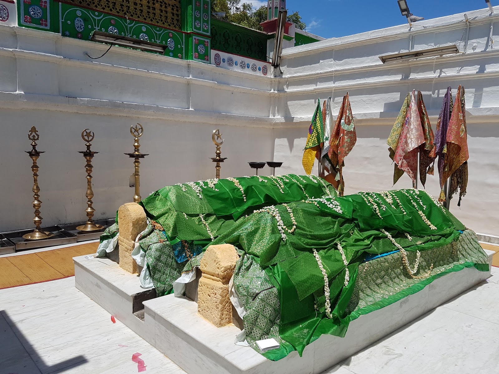 The white painted shrine interior. The ceiling is open and the tombs are covered in green cloths, with banners standing over the head of the tombs.